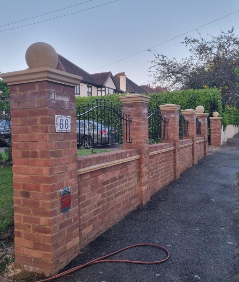 Brick wall with pillars and a gate, lined along a paved pathway in a residential area.