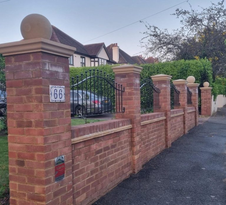 Brick wall with pillars and a gate, lined along a paved pathway in a residential area.
